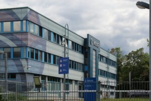 Bürogebäude der MEWA in Jena mit einem unverwechselbaren Design und einem eingezäunten Eingang; Ein berufliches oder unternehmerisches Umfeld; Das Gebäude verfügt über eine grau-blaue Fassade mit dem "Mewa"-Logo